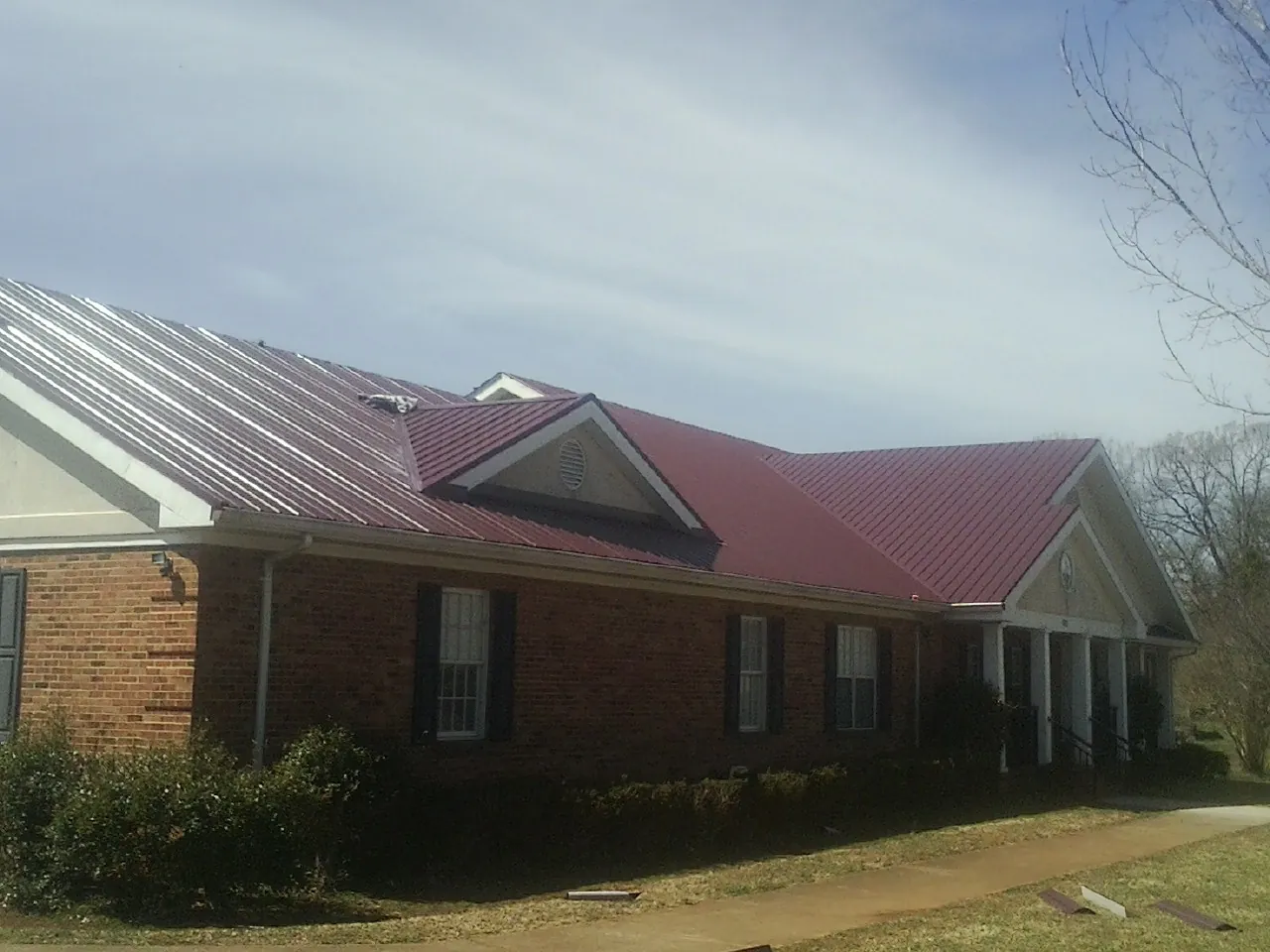 Red metal roof with gabled entries on a long brick building, from a Hail Damage Roof Repair job in Sterrett