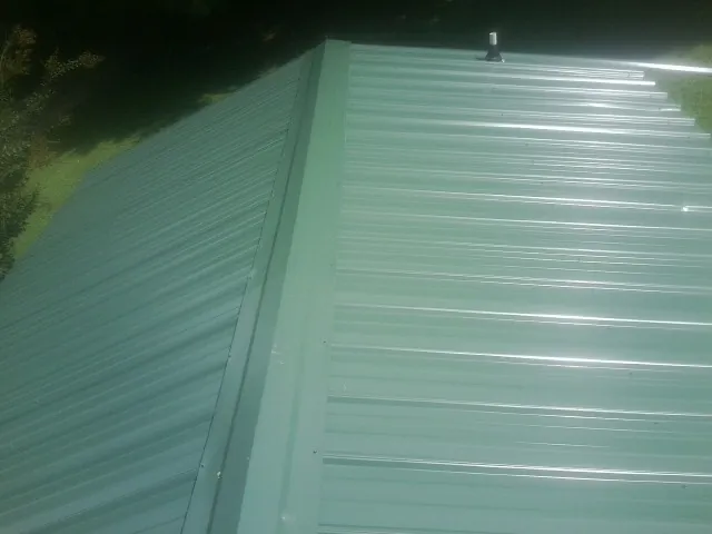 New green metal panels meeting at the ridge of a roof — Flat Roof Repair work by our crew in Sterrett