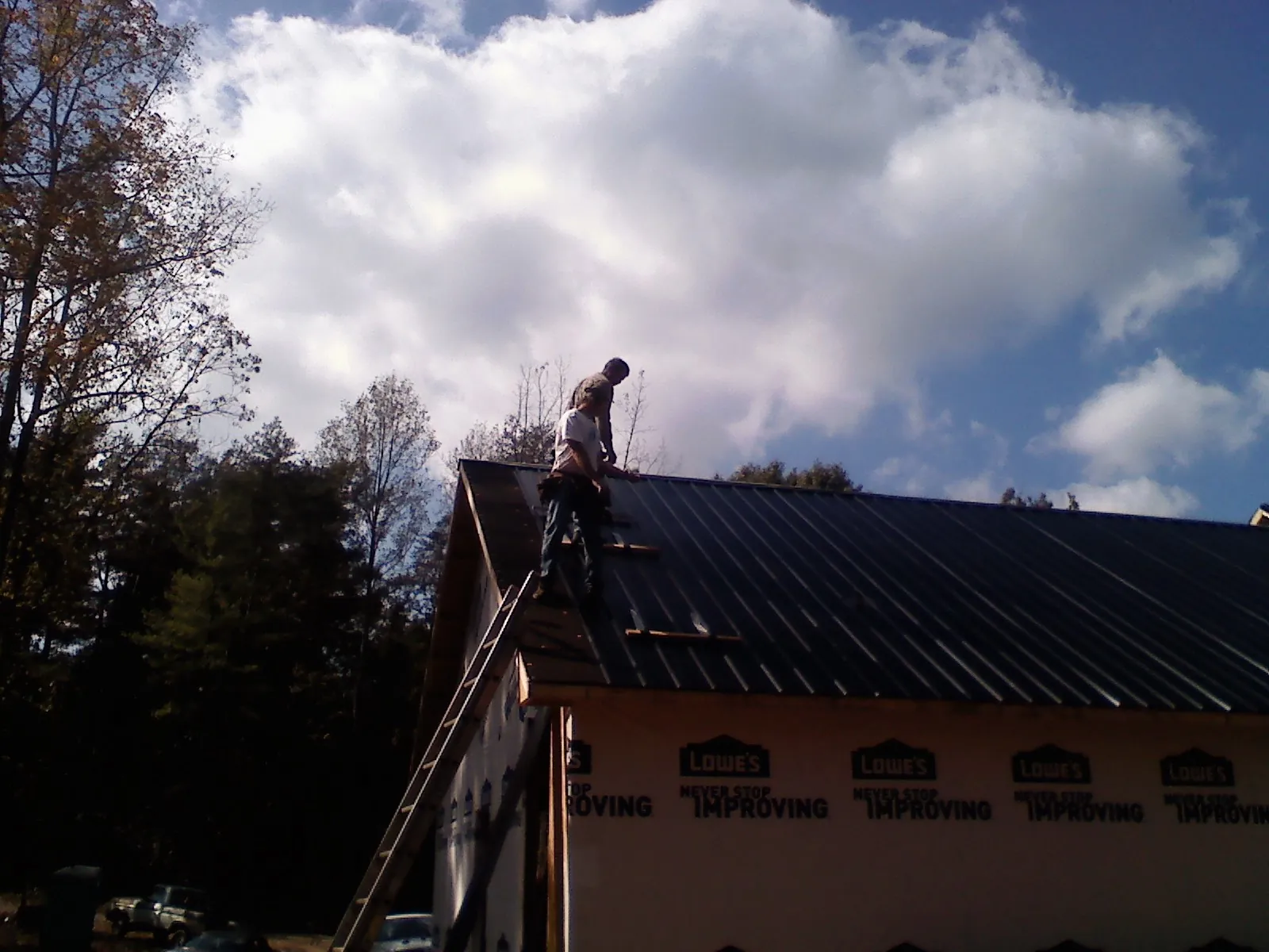 Roofer fastening dark metal panels high against a cloudy sky, from a Roof Inspection job in Sterrett