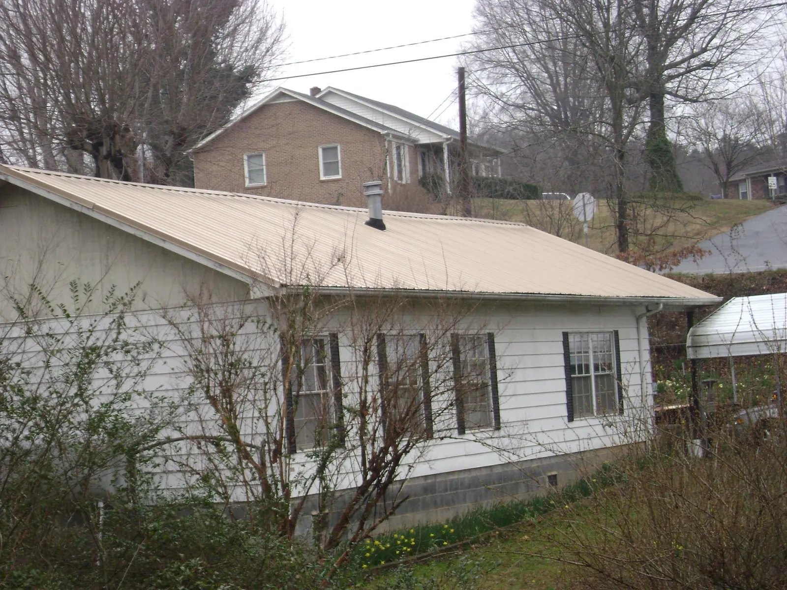 Tan metal roof on a white sided house set into a hillside — Commercial Roofing by Roofing Brothers in Sterrett