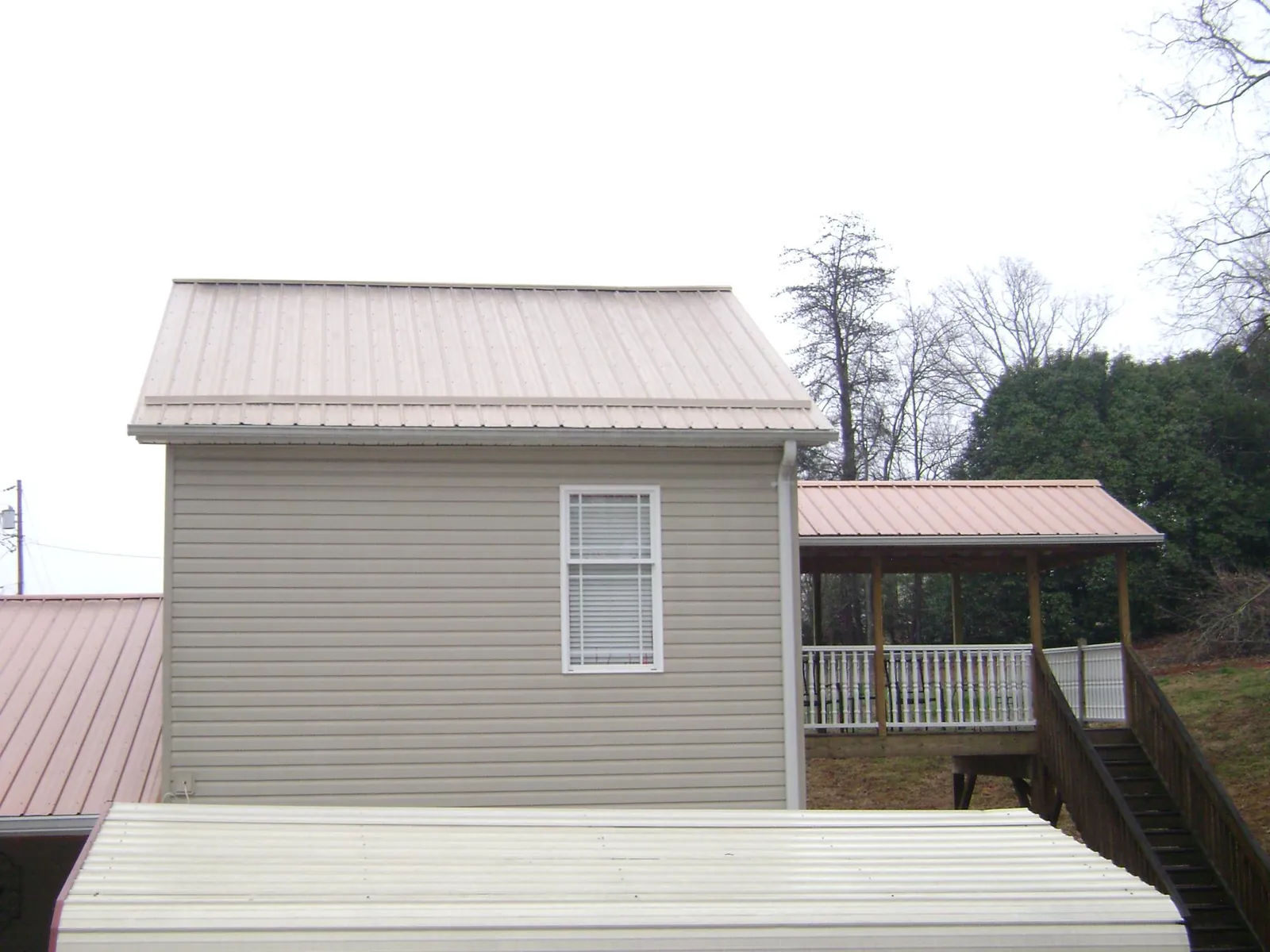 Tan metal roofs on a two story addition and attached porch, from a Roof Replacement job in Sterrett
